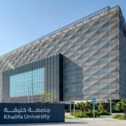 A huge grey building of Khalifa university and sidewalk, palm trees and gardens.